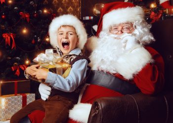 Santa Claus and shouting cute boy sitting in Christmas room with gifts. Christmas home decoration.